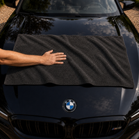 Serviette microfibre dépliée en travers du capot d'une berline noire, une main posée dessus pour l'échelle