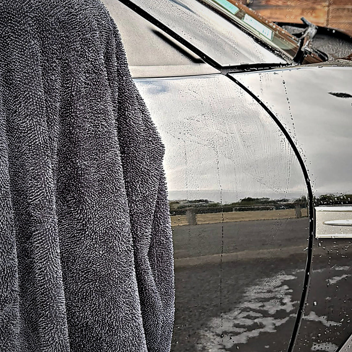 Serviette de séchage MIRE drapée sur l'aile d'une voiture noire encore mouillée