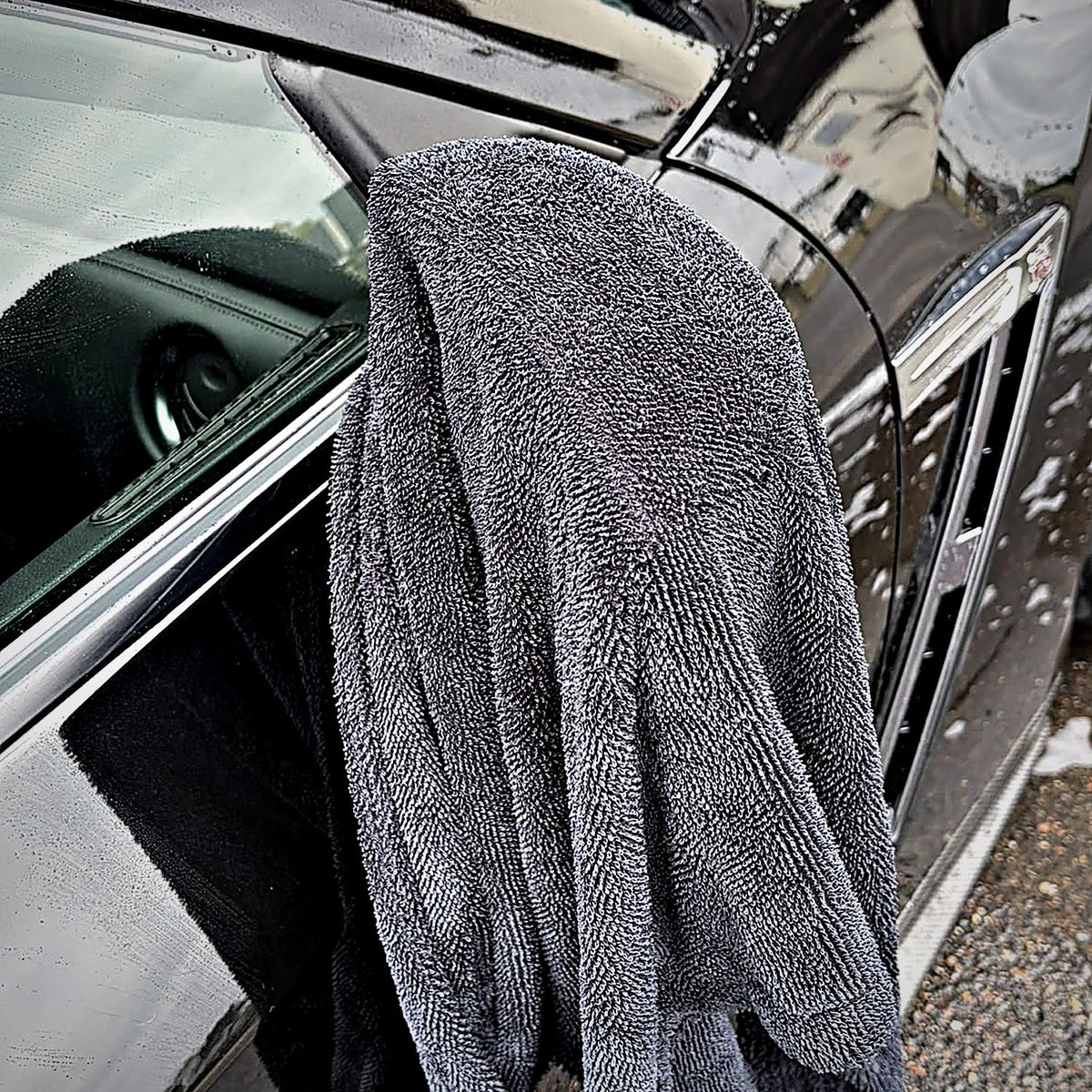 Serviette microfibre MIRE sur le flanc d'une voiture noire, près du rétroviseur